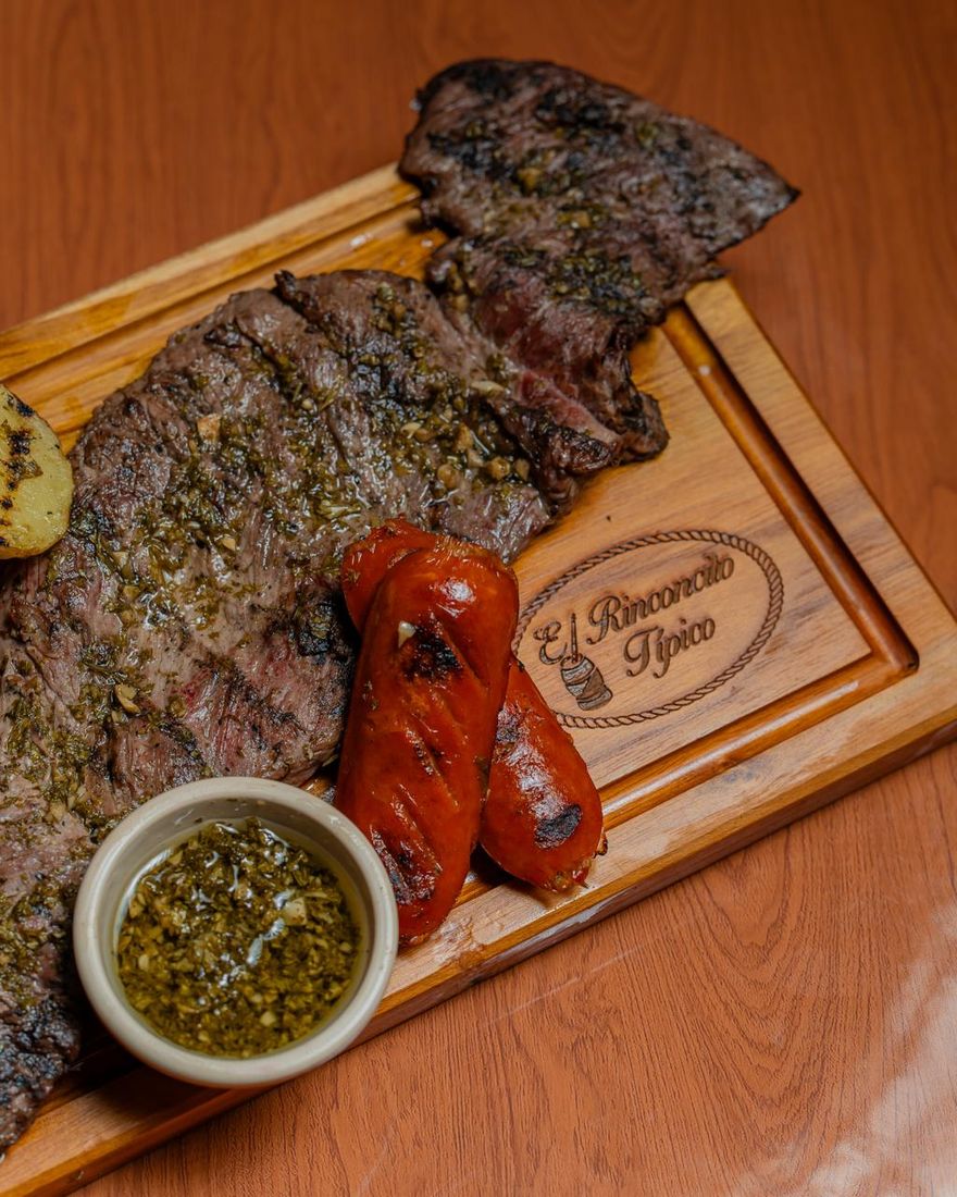 Churrasco con chimichurri y chorizo sobre una tabla con el logo de El Rinconcito Típico